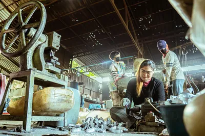 Industrial workers operating machinery in a factory setting, showcasing teamwork and manual labor.