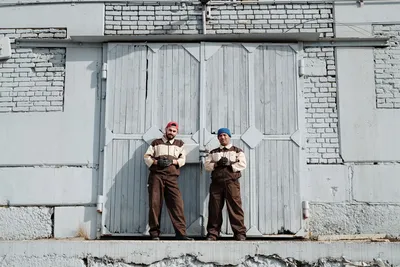 Two industrial workers pose confidently in front of a warehouse door, showcasing teamwork and uniformity.
